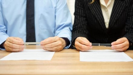 man and woman holding a pen in front of a divorce contract